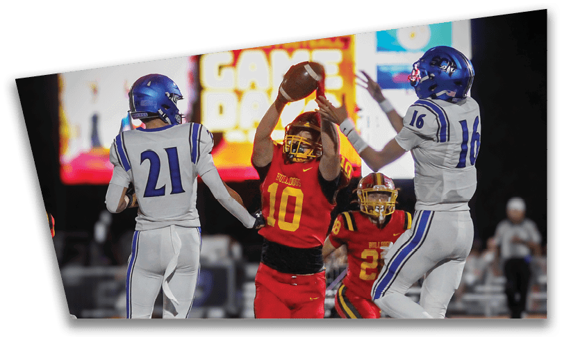 People wearing black American Canyon football uniforms and helmets are standing on a football field at night. Description generated by AI