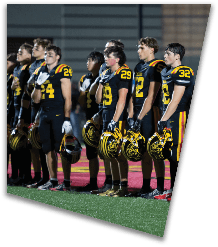 A person wearing a dark football uniform and helmet with “American Canyon" on the jersey is kneeling on one knee on a field at night. Description generated by AI