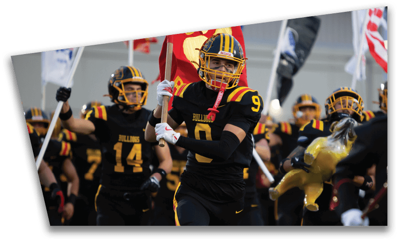 People wearing black American Canyon football uniforms and helmets are standing on a football field at night. Description generated by AI