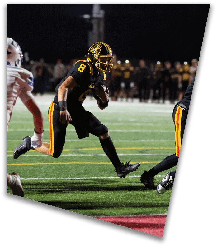 A person wearing a dark football uniform and helmet with “American Canyon" on the jersey is kneeling on one knee on a field at night. Description generated by AI