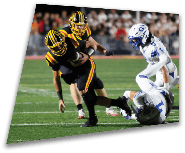 Four people in dark football uniforms and helmets stand in a row on a field, appearing focused and ready for action. Description generated by AI