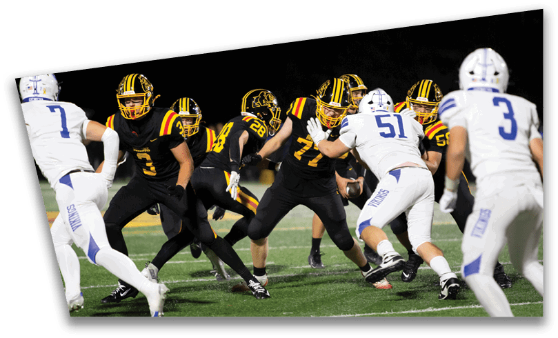 People wearing black American Canyon football uniforms and helmets are standing on a football field at night. Description generated by AI