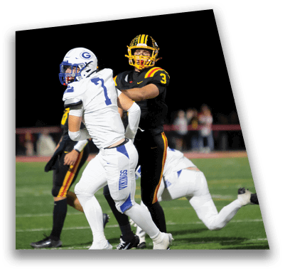 A person in football gear and helmet is crouched on a field with other players lined up in the background during a game. Description generated by AI