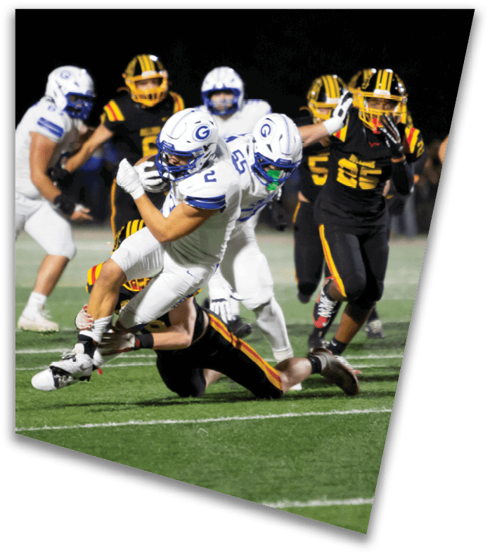 A person wearing a dark football uniform and helmet with “American Canyon" on the jersey is kneeling on one knee on a field at night. Description generated by AI
