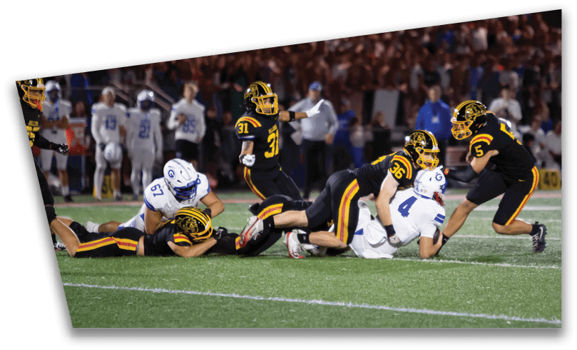 People wearing black American Canyon football uniforms and helmets are standing on a football field at night. Description generated by AI