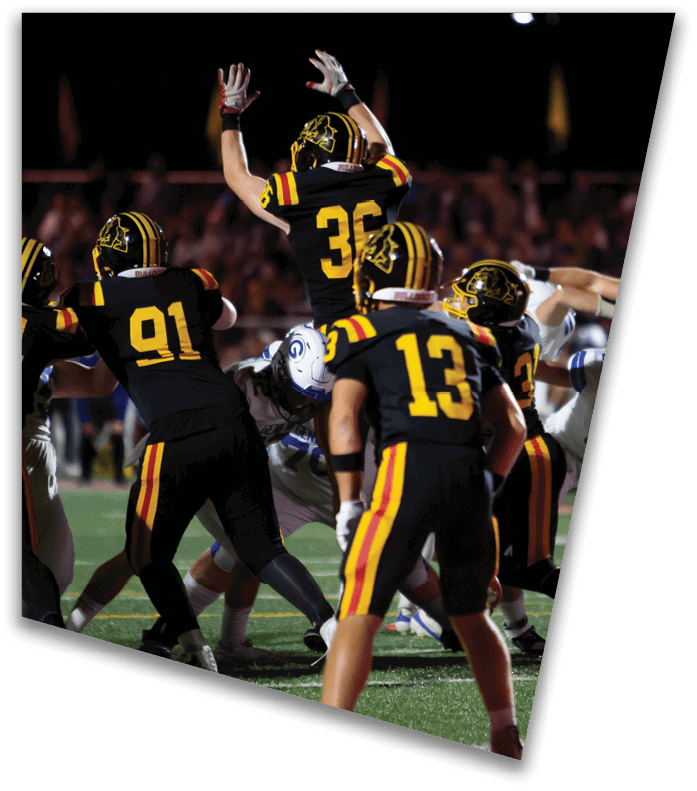 A person wearing a dark football uniform and helmet with “American Canyon" on the jersey is kneeling on one knee on a field at night. Description generated by AI