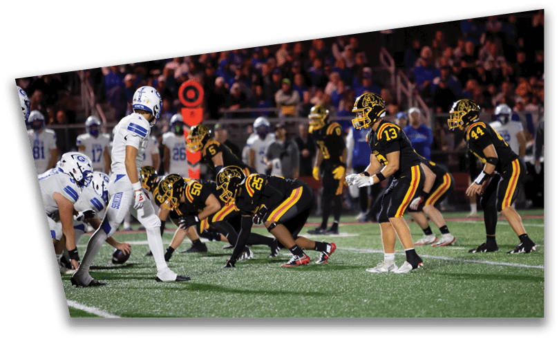 People wearing black American Canyon football uniforms and helmets are standing on a football field at night. Description generated by AI