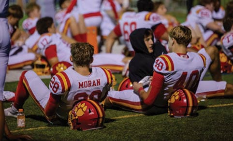 Two men wearing football uniforms are hugging each other on a field. AI generated content