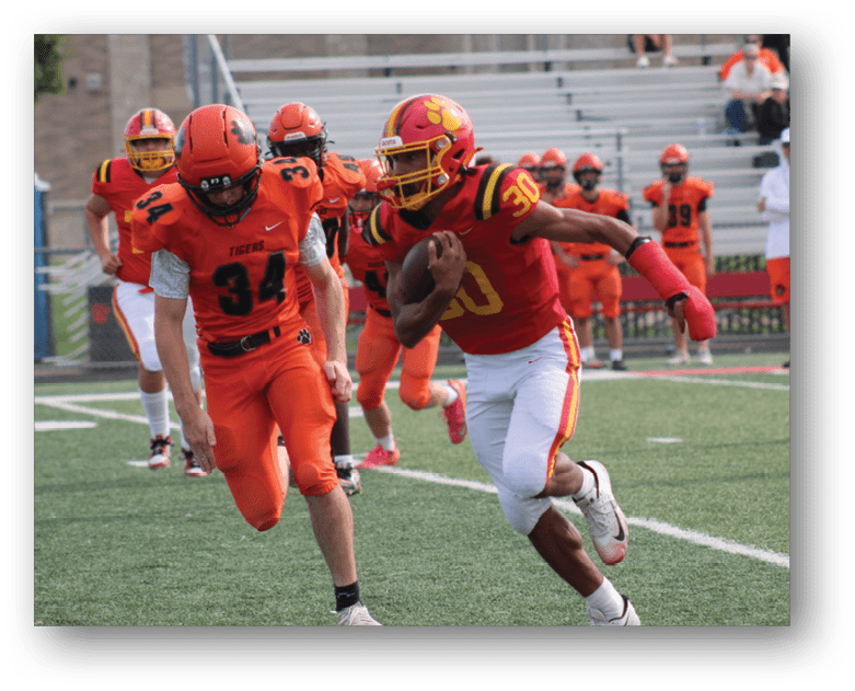 Three football players in blue and white uniforms running on a field. Description generated by AI