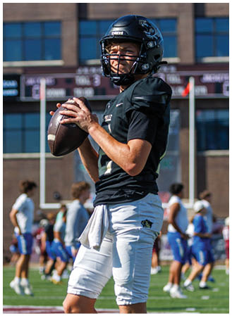 A football player in a black jersey holding a football. Description generated by AI