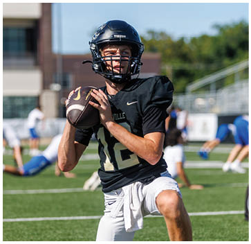 A football player kneeling on the field holding a football. Description generated by AI