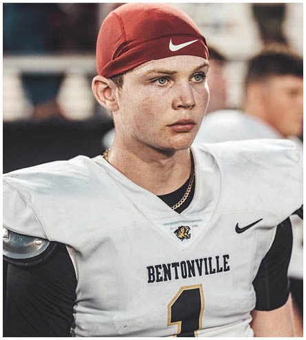 A football player wearing a red hat and a white jersey with the word Bentonville on it. Description generated by AI