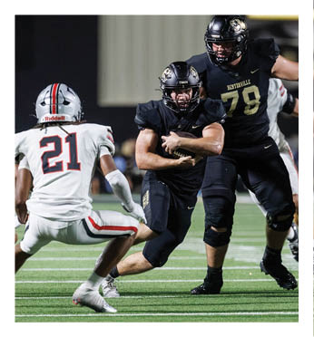A football player in a black jersey is tackled by another player. Description generated by AI