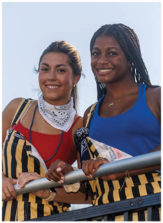 Two women wearing striped shirts and holding a hot dog. Description generated by AI
