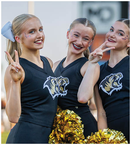 Three cheerleaders in black and yellow uniforms with yellow pom poms. Description generated by AI