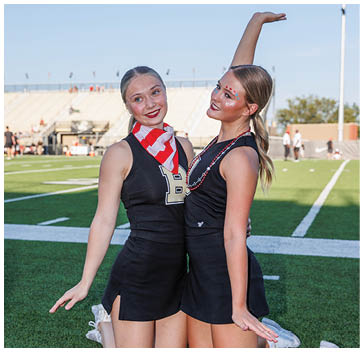 Two cheerleaders wearing black and white uniforms. Description generated by AI