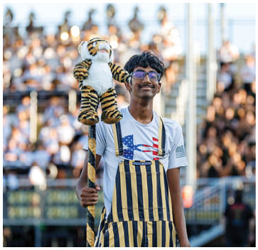 A man wearing a white shirt and blue and yellow pants holding a stuffed tiger. Description generated by AI