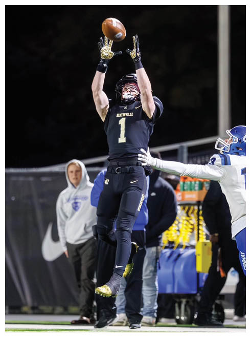 A football player wearing a black jersey with the number 1 on it leaps in the air to catch a football. Description generated by AI