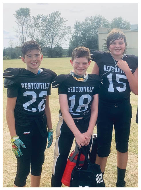 Three boys wearing football uniforms. Description generated by AI