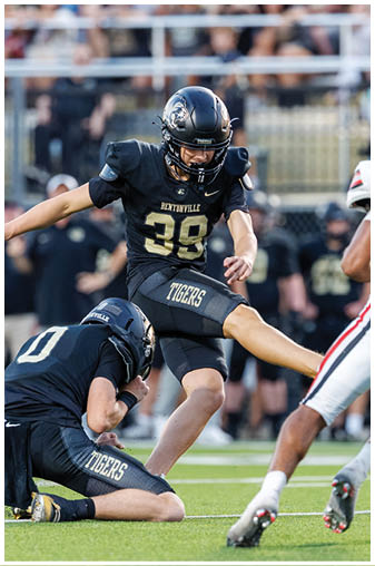 A soccer player in a black and gold uniform kicks the ball. Description generated by AI