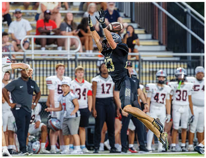 A football player in a black jersey catching a football. Description generated by AI