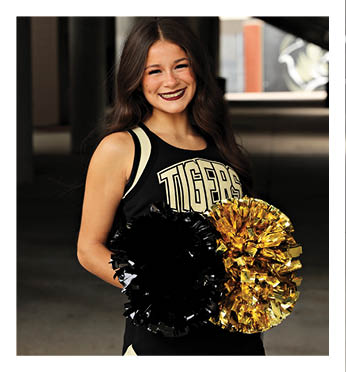 A cheerleader for the Tigers holds a yellow and black pom pom. Description generated by AI