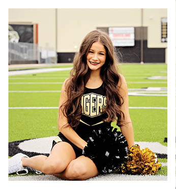 A cheerleader with a yellow and black uniform is sitting on the grass. Description generated by AI