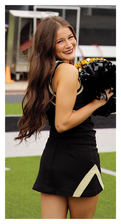A cheerleader in a black and white uniform holding a pom pom. Description generated by AI