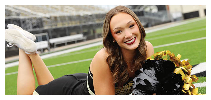 A cheerleader is laying on the ground holding a black and gold pom pom. Description generated by AI