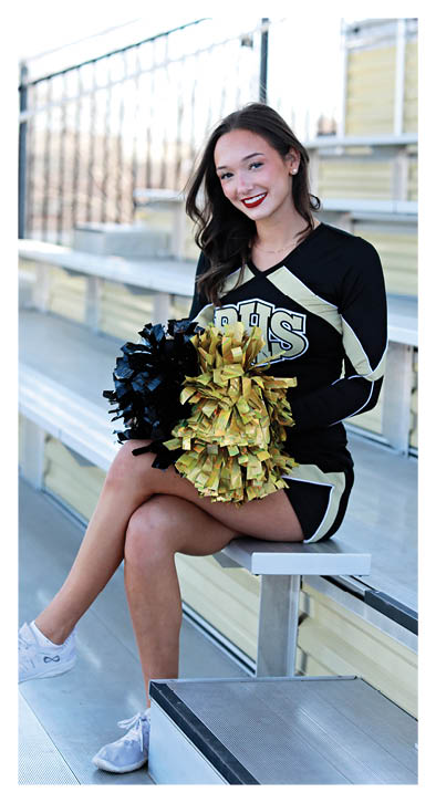 A cheerleader in a black and gold uniform sits on a bench. Description generated by AI