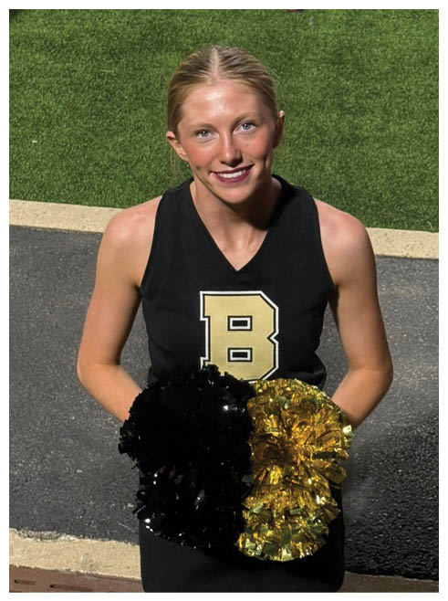 A cheerleader wearing a black and yellow uniform and holding a pom pom. Description generated by AI