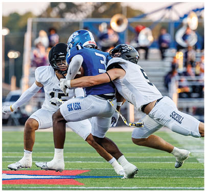 A football player in a white jersey is tackled by another player. Description generated by AI