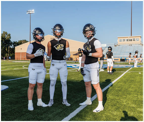 Three football players standing on a field. Description generated by AI
