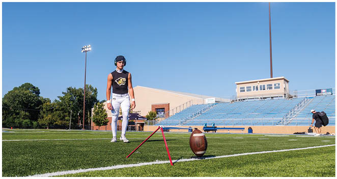 A football player is standing on a field with a football in front of him. Description generated by AI