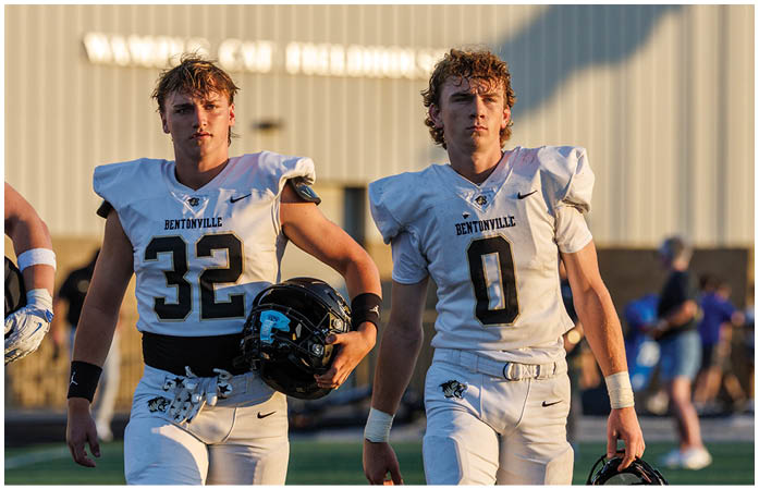 Two football players wearing white and black uniforms. Description generated by AI