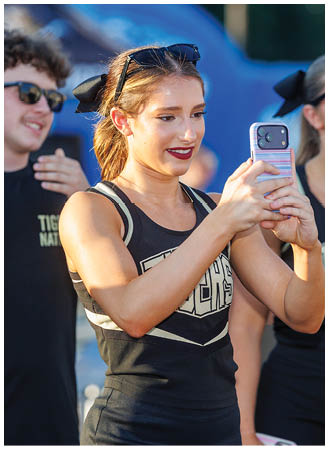 A woman in a black and gold uniform is taking a picture of herself with her cell phone. Description generated by AI