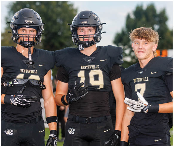 Three football players standing on a field. Description generated by AI