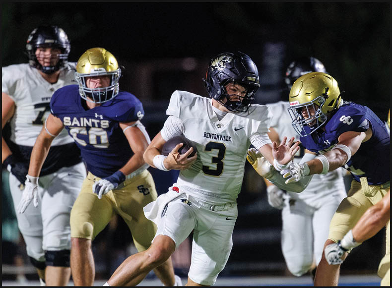 Four people wearing black football uniforms with “VISTA" on the front are standing together in a stadium with a crowd in the background, two of them holding helmets raised above their heads. Description generated by AI