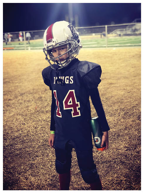 A young boy wearing a football uniform and holding a water bottle. Description generated by AI