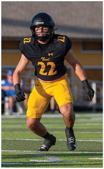 An adult wearing a black football jersey with the number 22 and yellow pants is running on a football field. Descripci n generada con IA