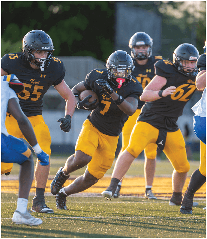 Several people wearing black and yellow football uniforms are actively playing on a field during a game, with one person running while holding the ball. Descripci n generada con IA