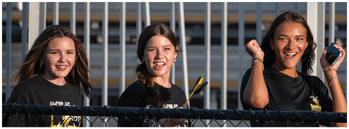 Three adults wearing black shirts are standing behind a fence with metal bars, smiling and appearing engaged in an outdoor setting. Descripci n generada con IA