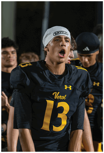 A person wearing a black football jersey with the number 13 and a white headband is shouting or cheering while standing among other people in similar jerseys. Descripci n generada con IA