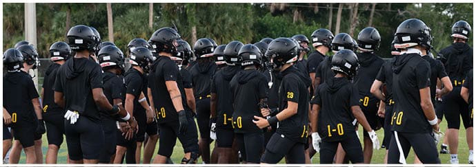 A group of people wearing black sports uniforms and helmets are gathered on a grassy field, appearing to prepare for or participate in a team activity. Descripci n generada con IA