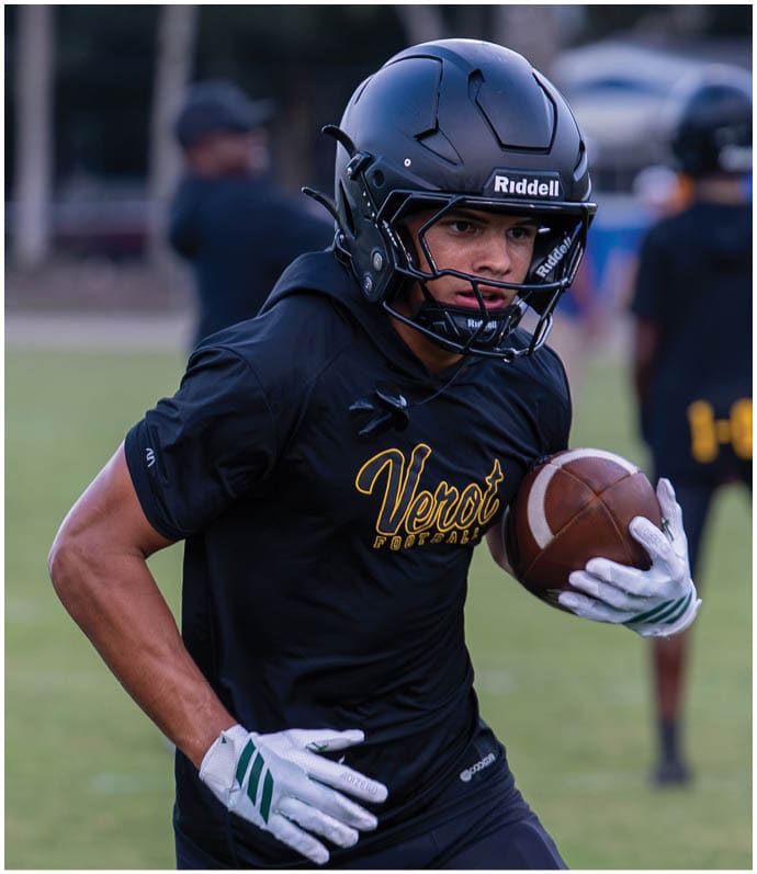 A person wearing a black football helmet and black shirt with “Venot" written on it is running on a field while holding a football. Descripci n generada con IA