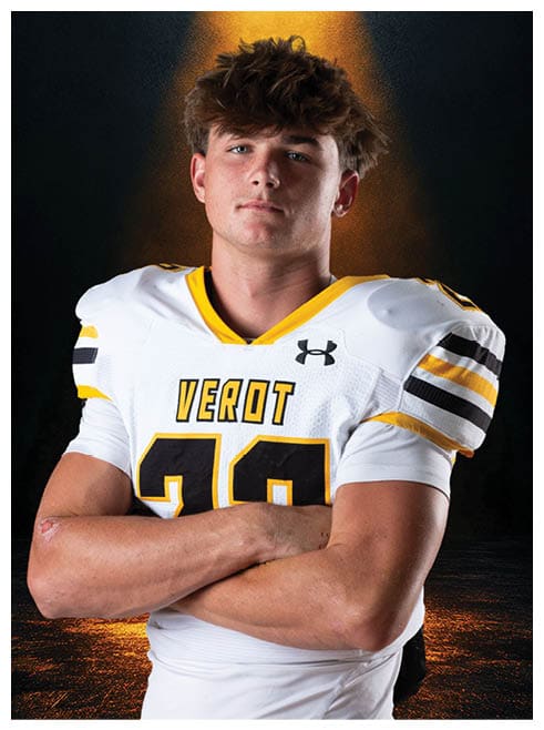 A person with short tousled hair wearing a white sports jersey with yellow and black accents is shown from the shoulders up against a dark background with a warm light gradient. Descripci n generada con IA