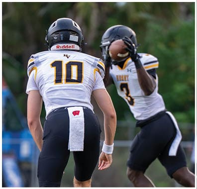Two people in football uniforms are on a field with one preparing to throw a football and the other facing them wearing a jersey with the number 10. Descripci n generada con IA