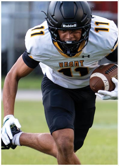 A person wearing a black helmet and white football jersey with the number 11 is running on a field while holding a football. Descripci n generada con IA