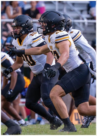 Several people in football uniforms and helmets are crouched and poised on a field, appearing ready to start a play. Descripci n generada con IA