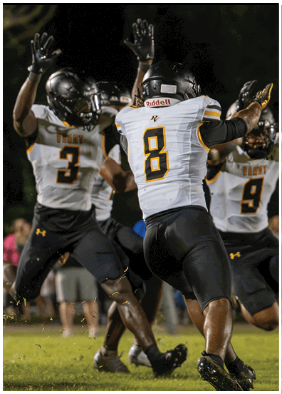Three people in football uniforms with helmets are celebrating on a grassy field at night. Descripci n generada con IA